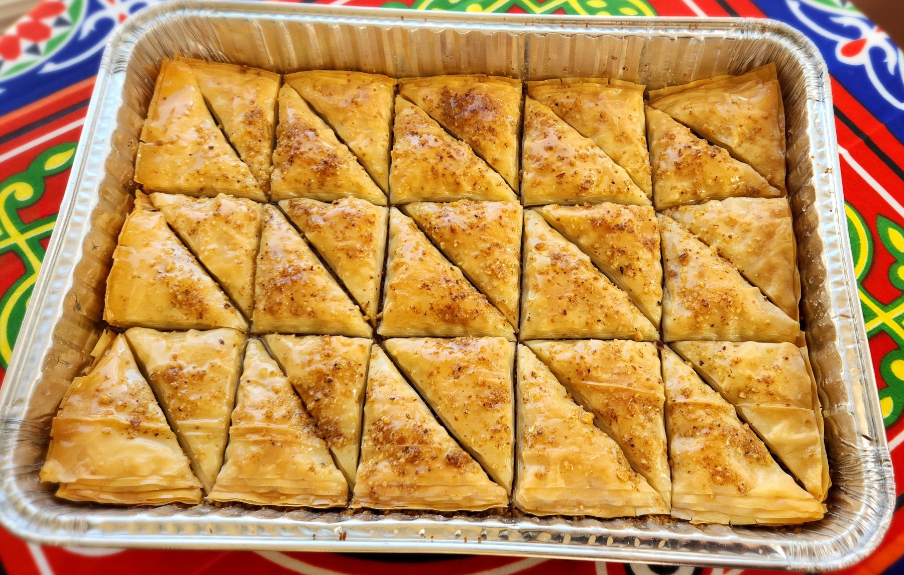 A foil tray of freshly cut baklava pieces on a colorful patterned cloth