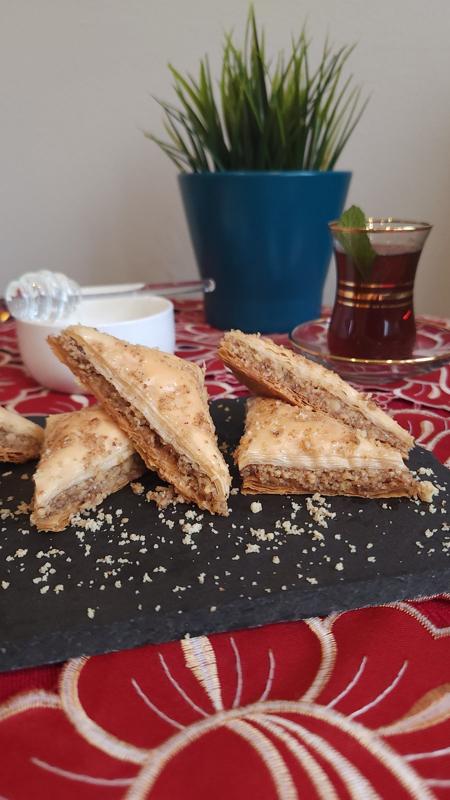 Baklava triangles piled on a slate board over a red embroidered cloth